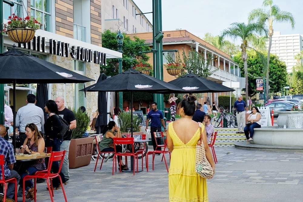 Photograph of a women in yellow walking outside of the Little Italy Food Hall